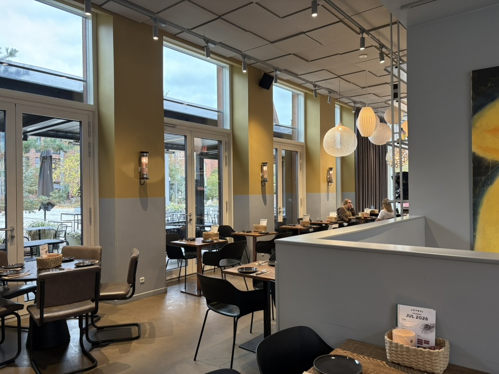 Indretningen hos café AKTUEL på Budolfi Plads i Aalborg med store vinduer, moderne møbler og lyse lokaler.