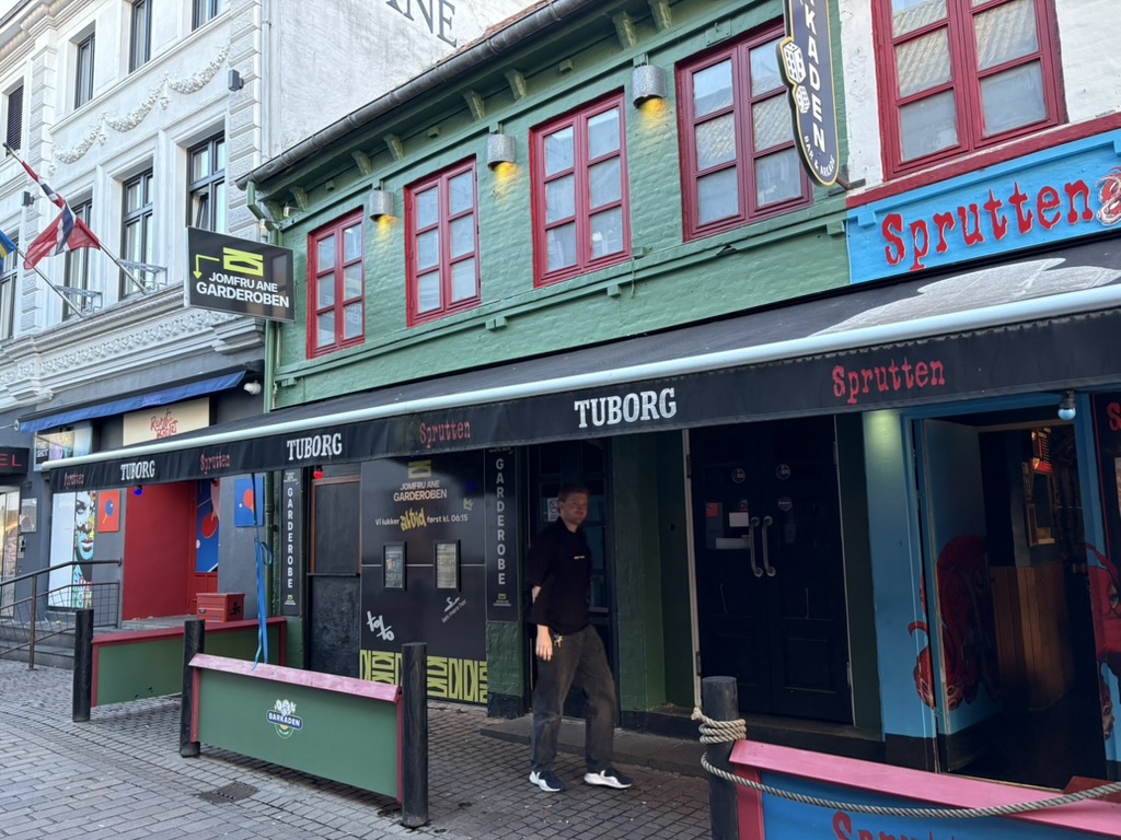 Facaden på Sprutten i Jomfru Ane Gade i Aalborg med grøn bygning, røde vinduer og Tuborg-markiser.