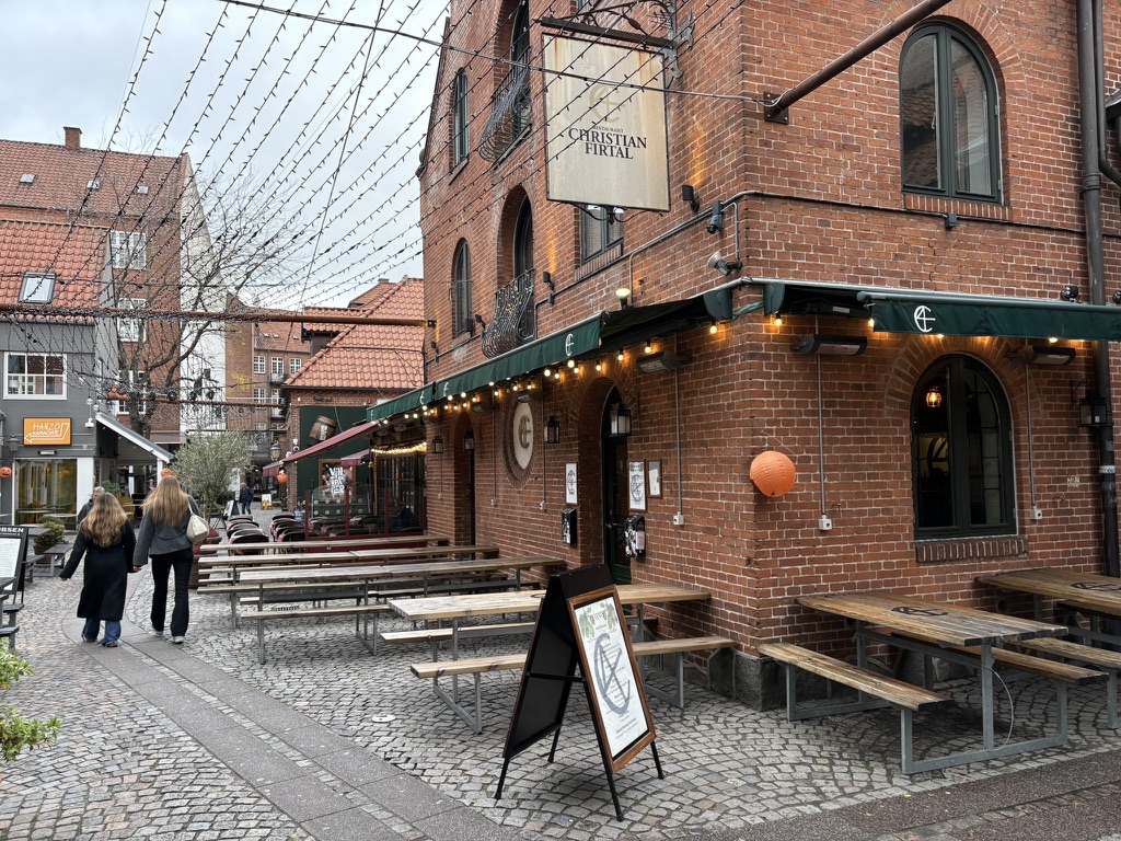 Christian Firtal i Vintapperstræde i Odense med karakteristisk murstensfacade, grønne markiser og udendørs borde og bænke.